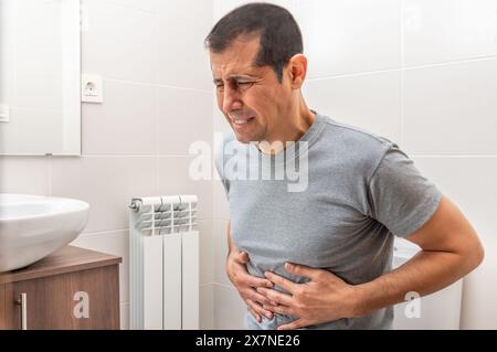 Colpo corto di un uomo seduto sul gabinetto in un bagno da solo e che soffre di crampi allo stomaco mentre si è a casa da solo Foto Stock