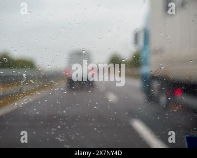 Piacenza, Italia - 22 aprile 2024 Una scena autostradale sotto un cielo coperto con auto e camion con segnaletica stradale e un cavalcavia, giornata di pioggia su Motorwa Foto Stock