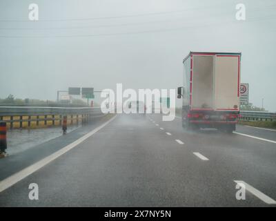 Piacenza, Italia - 22 aprile 2024 Una scena autostradale sotto un cielo coperto con auto e camion con segnaletica stradale e un cavalcavia, giornata di pioggia su Motorwa Foto Stock