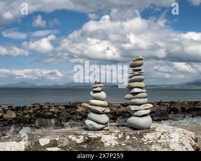 Pietre Zen bilanciate su una grande roccia su una spiaggia gallese in una splendida giornata primaverile con le montagne della penisola di Llyn e il mare sullo sfondo Foto Stock