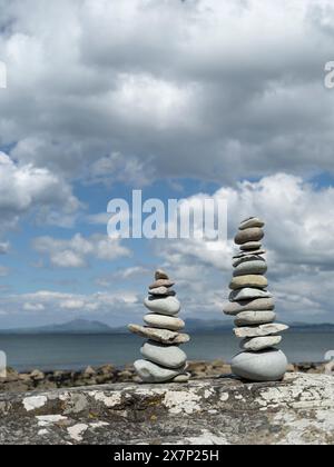 Pietre Zen bilanciate su una grande roccia su una spiaggia gallese in una splendida giornata primaverile con le montagne della penisola di Llyn e il mare sullo sfondo Foto Stock