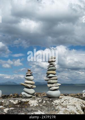 Pietre Zen bilanciate su una grande roccia su una spiaggia gallese in una splendida giornata primaverile con le montagne della penisola di Llyn e il mare sullo sfondo Foto Stock