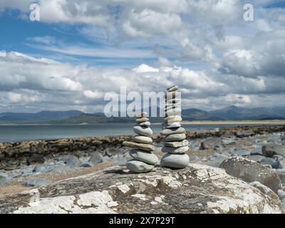 Pietre Zen bilanciate su una grande roccia su una spiaggia gallese in una splendida giornata primaverile con le montagne della penisola di Llyn e il mare sullo sfondo Foto Stock
