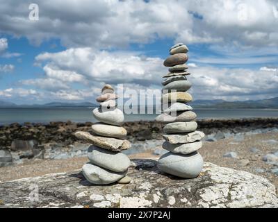 Pietre Zen bilanciate su una grande roccia su una spiaggia gallese in una splendida giornata primaverile con le montagne della penisola di Llyn e il mare sullo sfondo Foto Stock