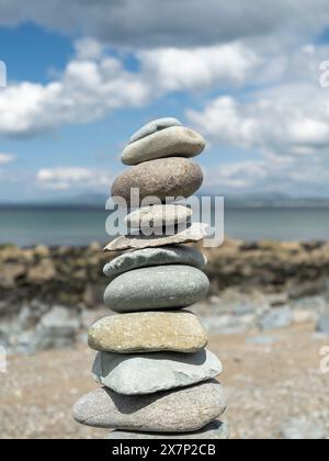 Pietre Zen bilanciate su una grande roccia su una spiaggia gallese in una splendida giornata primaverile con le montagne della penisola di Llyn e il mare sullo sfondo Foto Stock