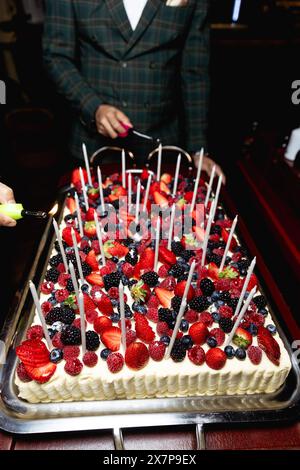 Una torta alla frutta di compleanno con tante piccole candele. Una torta con fragole fresche. Accendere le candele sulla torta. Foto Stock