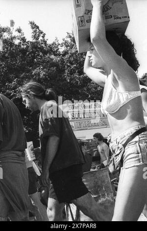 AREA RISTORO, FOLLA, ONDE DI CALORE, PALCOSCENICO NME, GLASTONBURY 95: una donna in bikini e pantaloncini denim porta una scatola sulla testa attraverso l'area delle bancarelle nell'estrema ondata di caldo estivo vicino al secondo NME Stage Field e alla folla al Glastonbury Festival, Pilton Farm, Somerset, Inghilterra, 24 giugno 1995. Nel 1995 il festival ha celebrato il suo 25 ° anniversario. Molte persone hanno lottato con il colpo di calore nel weekend particolarmente caldo. Foto: ROB WATKINS Foto Stock