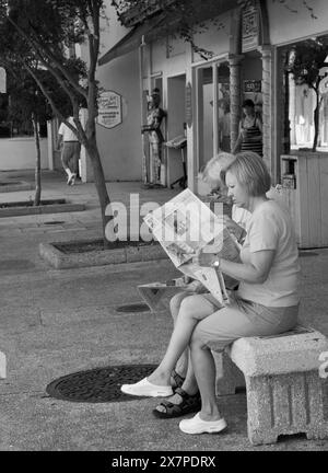 Un uomo e una donna che leggono un giornale mentre riposano in St. George Street a St. Augustine, Florida, USA. Foto Stock