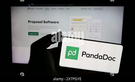 Persona che possiede uno smartphone con il logo della società statunitense PandaDoc Inc. Di fronte al sito Web. Mettere a fuoco il display del telefono. Foto Stock