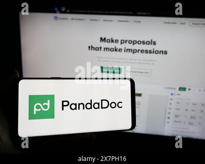 Persona che possiede un telefono cellulare con il logo della società americana di software per l'automazione dei documenti PandaDoc Inc. Davanti al sito web. Mettere a fuoco il display del telefono. Foto Stock