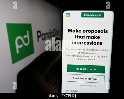 Persona che detiene un cellulare con pagina web della società statunitense PandaDoc Inc. Di fronte al logo. Messa a fuoco al centro del display del telefono. Foto Stock