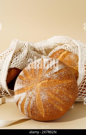 Pane artigianale a pasta madre con crosta dorata, esposto in un sacchetto di panno ecologico su sfondo beige. Foto Stock