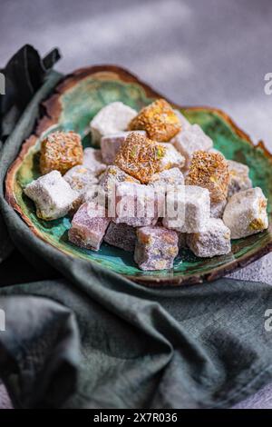 Un assortimento di colorate delizie turche tradizionali presentate su un piatto di ceramica, accompagnate da tè nero in un bicchiere e da un vaso di rose bianche Foto Stock