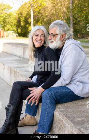 Un'affettuosa coppia di anziani condivide risate e momenti intimi mentre si siede su una panchina in un tranquillo parco, mostrando la bellezza della matur Foto Stock