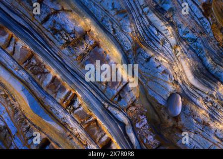 Vista aerea astratta di formazioni rocciose testurizzate con intricate laminazioni e un ciottolo solitario, evidenziato da colori contrastanti in luce naturale. Foto Stock