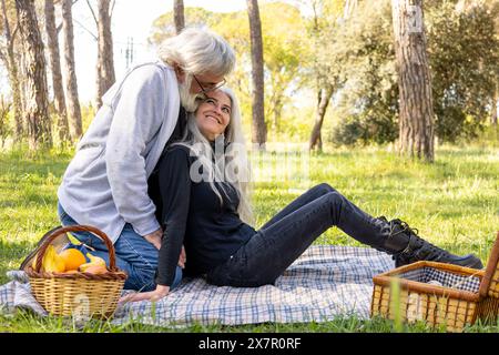 Una coppia senior condivide un momento tenero durante un romantico picnic in un parco erboso, completo di un cestino da picnic pieno di frutta Foto Stock