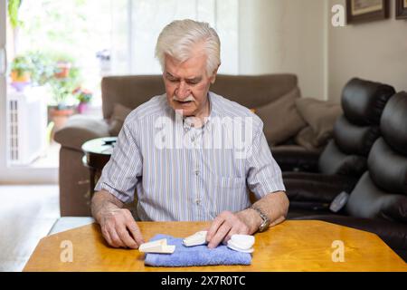 Un anziano uomo dai capelli bianchi si siede a un tavolo, controllando il livello di zucchero nel sangue con un glucometro che sembra concentrato e preoccupato, sottolineando il importa Foto Stock