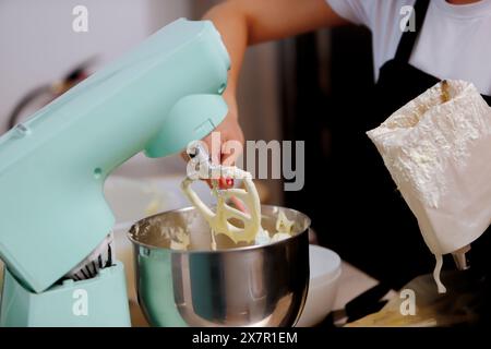 Una persona che cuoce una torta versa la farina in un recipiente di miscelazione mentre un moderno mixer color acqua mescola gli ingredienti insieme Foto Stock
