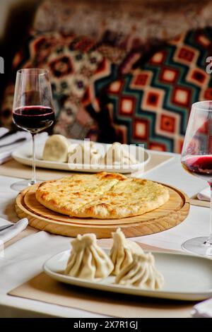 Un'allettante selezione di cucina georgiana con Khachapuri, Khinkali e vino servito su una tavola di legno e piatti tradizionali Foto Stock