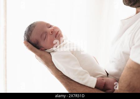 Un bambino appena nato tranquillo dorme pacificamente mentre è cullato tra le braccia di supporto di un genitore, mostrando un momento di pura innocenza e amore Foto Stock
