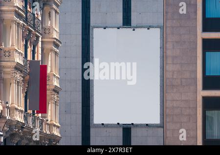 Un cartellone vuoto è appeso su un edificio moderno accanto a una facciata di architettura classica a Madrid, perfetto per i mockup pubblicitari Foto Stock