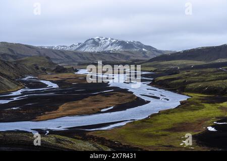 Un tranquillo fiume si snoda attraverso le valli verdeggianti e le colline vulcaniche degli altopiani islandesi, mostrando lo splendore della natura Foto Stock