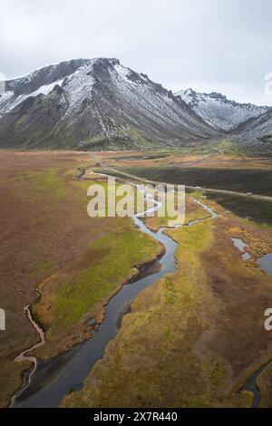 Una tranquilla ripresa aerea cattura un fiume serpeggiante che si snoda attraverso un vasto paesaggio montuoso con montagne innevate Foto Stock