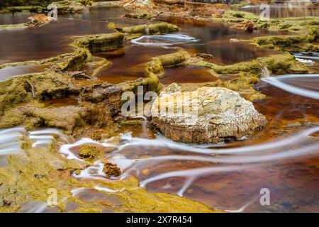 Scatto a lunga esposizione che cattura le vorticose acque e le vibranti formazioni rocciose gialle del fiume Riotinto, mettendo in evidenza i depositi minerali naturali e la S. Foto Stock