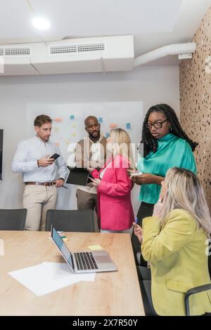 Gruppi diversi di professionisti che collaborano in uno spazio di coworking ben illuminato con un computer portatile e appunti sulla parete Foto Stock