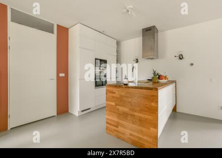 Questa immagine mostra una cucina contemporanea caratterizzata da eleganti mobili bianchi e un'isola centrale con un ripiano in legno. Il design minimalista è com Foto Stock