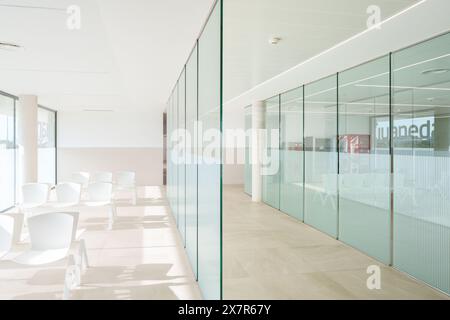 L'interno luminoso e pulito di una sala d'attesa dell'ospedale presenta un design minimalista con sedie bianche e pareti divisorie in vetro. Foto Stock