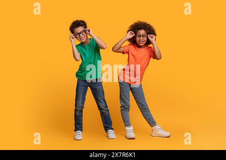 Due bambini allegri che fanno facce divertenti su sfondo giallo brillante Foto Stock