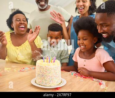 Famiglia multi-generazione che celebra il compleanno della nipote a casa con torta e festa Foto Stock