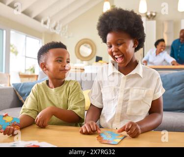 Ragazzo e ragazza che gioca a Game of Cards a casa con la famiglia Multi Generation in background Foto Stock