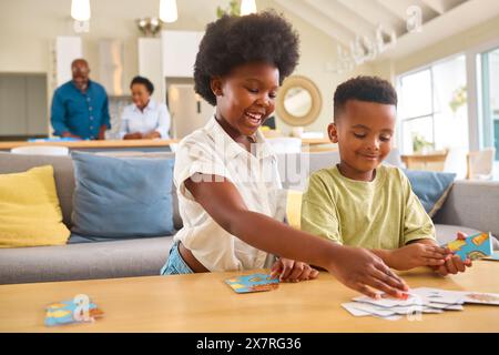 Ragazzo e ragazza che gioca a Game of Cards a casa con la famiglia Multi Generation in background Foto Stock