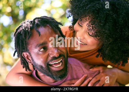 Coppia di adulti adulti innamorati all'aperto nel giardino estivo o in campagna con Piggyback Man Giving Woman Foto Stock