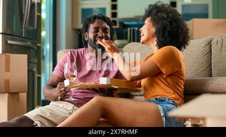 Giovane coppia che festeggia a New Home il giorno del trasloco mangiando pizza e bevendo vino Foto Stock