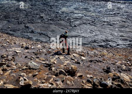 Turista donna con zaino in piedi sulla cima delle rocce di basalto fuso nel campo di lava del vulcano Fagradalsfjall, osservando il paesaggio vulcanico dell'Islanda. Foto Stock