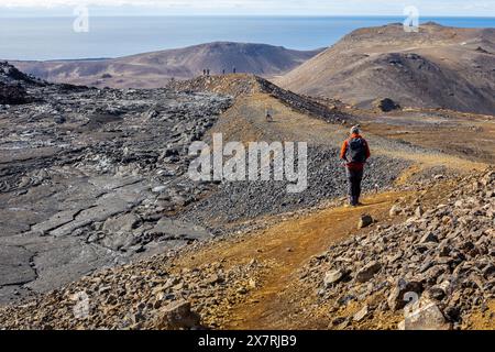 Turista maschile che cammina nel campo lavico del vulcano Fagradalsfjall, paesaggio ghiacciato di lava basaltica creato dopo l'eruzione, Islanda. Foto Stock