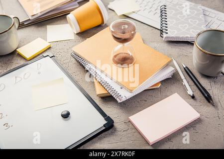 Il raccolto di clessidra sul tavolo dell'ufficio domestico misura il tempo. Luogo di lavoro di dipendenti impegnati, gestione del tempo e concetto di burnout Foto Stock