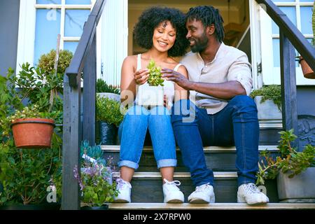 La coppia si siede sui gradini all'esterno di casa e si prende cura delle piante da giardino Foto Stock