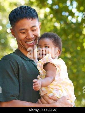 Foto in famiglia con amorevole padre Cuddling Baby Daughter all'aperto in giardino o in campagna Foto Stock