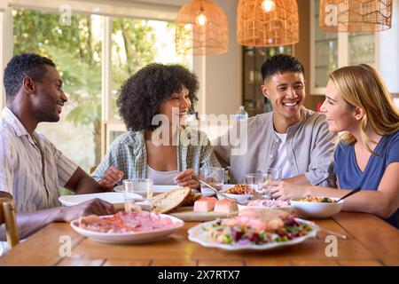 Gruppo di amici multirazziali seduti intorno al tavolo e gustati un pasto a casa insieme Foto Stock