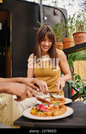 La donna di una coppia interrazziale affetta delicatamente nel suo pasto con un coltello e una forchetta durante un romantico pranzo in camper. Foto Stock