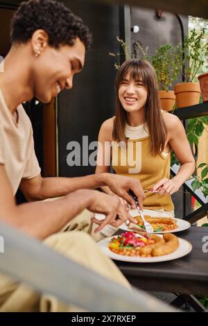 Una coppia interrazziale si gode un pasto accogliente in un camper, assaporando ogni boccone di cibo delizioso insieme. Foto Stock