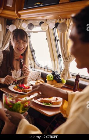 Un gruppo eterogeneo di amici si diverte a gustare un pasto condiviso e a conversare intorno a un tavolo carico di cibo. Foto Stock