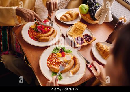 Una coppia interrazziale gode di un piacevole pranzo nel loro camper, circondato da piatti di cibo delizioso vicino a una finestra illuminata dal sole. Foto Stock