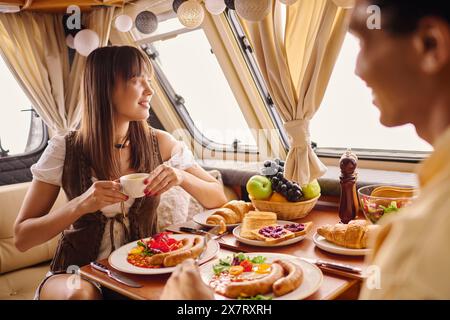 Una coppia interrazziale che gusta un delizioso pasto insieme in un accogliente camper, creando ricordi in una fuga romantica. Foto Stock