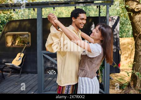 Un uomo e una donna di razze diverse ballano gioiosamente di fronte a una tenda colorata in un ambiente naturale. Foto Stock