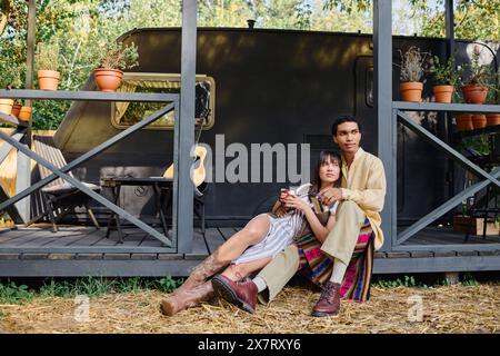 Un uomo e una donna interrazziali si siedono insieme per terra, facendo una pausa tranquilla durante la loro fuga romantica in un ambiente naturale. Foto Stock